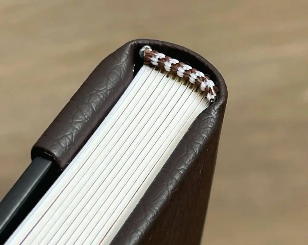 茶色い表紙の本の天側に、色糸のかがりと紙の小口が見える